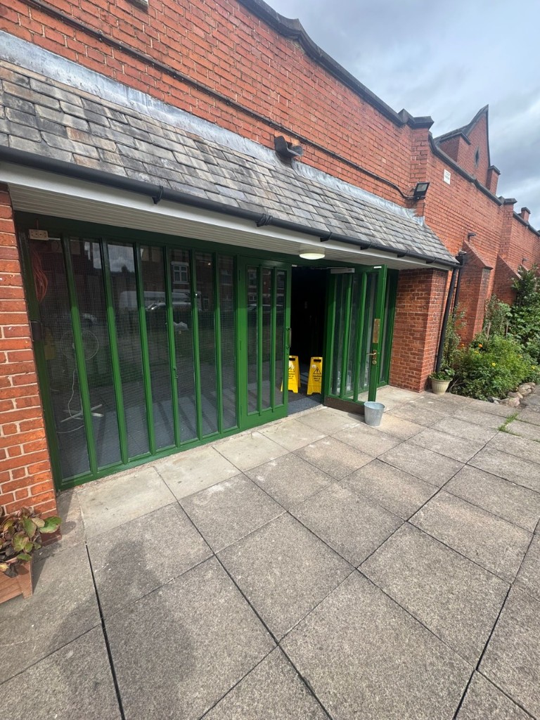 Exterior folding glass doors painted forest green on a red brick church building in Leicester