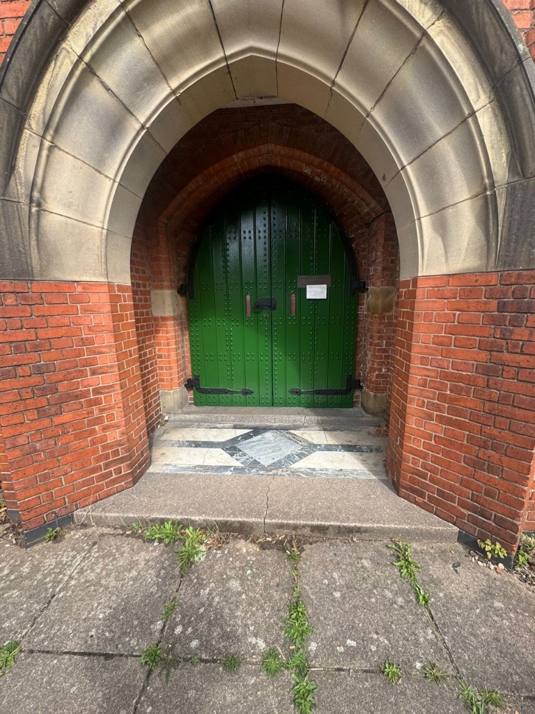 Freshly painted gloss green Gothic arched church doors set in a stone and brick entrance archway in Leicester