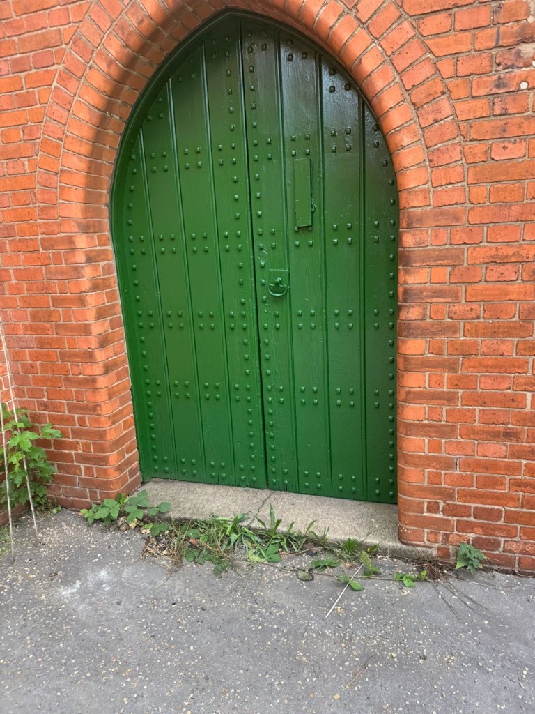 Studded arched timber church doors freshly painted gloss green against red brick