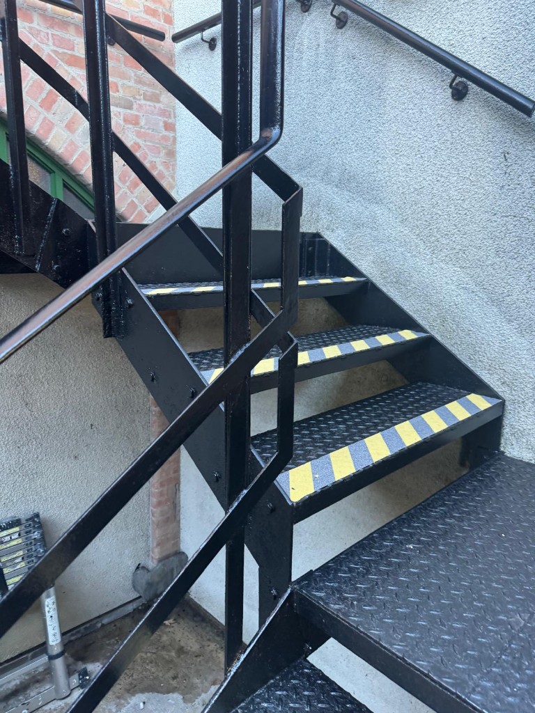 Turn of the steel staircase with freshly painted black balustrade and high-visibility step edges — after