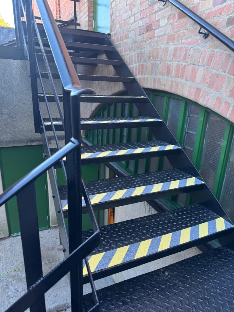 Upper flight of the steel staircase painted black with yellow and black anti-slip nosings — after