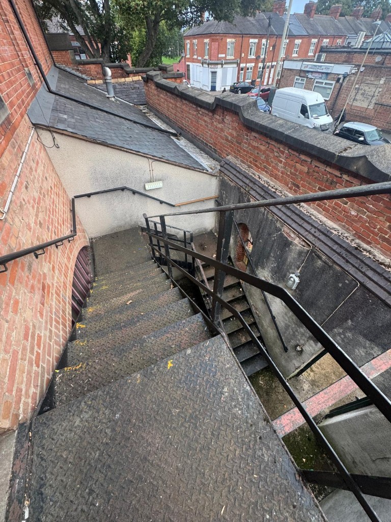 Looking down the steel staircase before work, with worn grey treads and moss on the steps