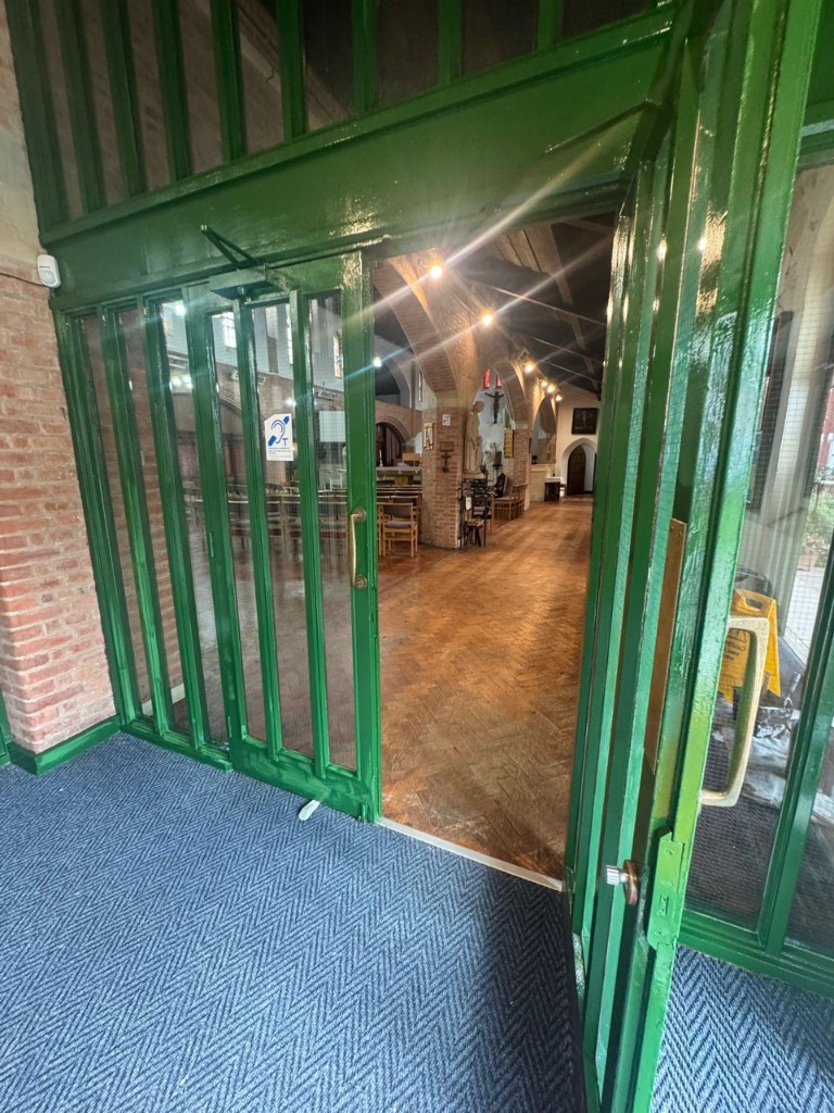 Green-painted interior glass doors looking through into a Leicester church hall with parquet flooring