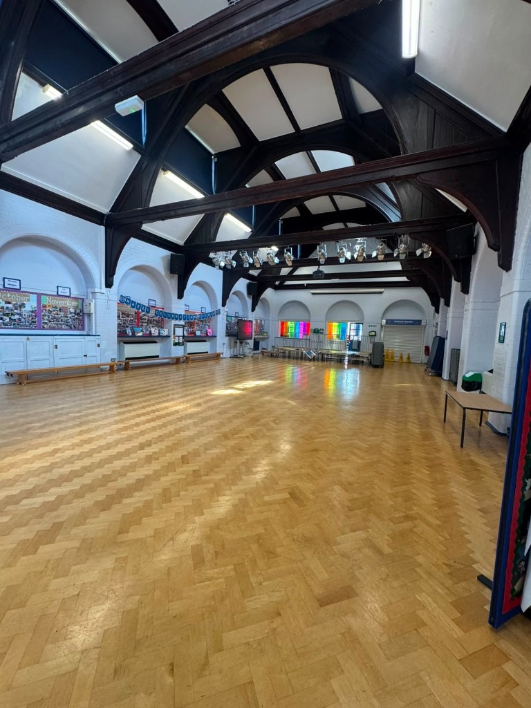 School assembly hall with white painted brick walls, vaulted timber roof and polished wooden floor