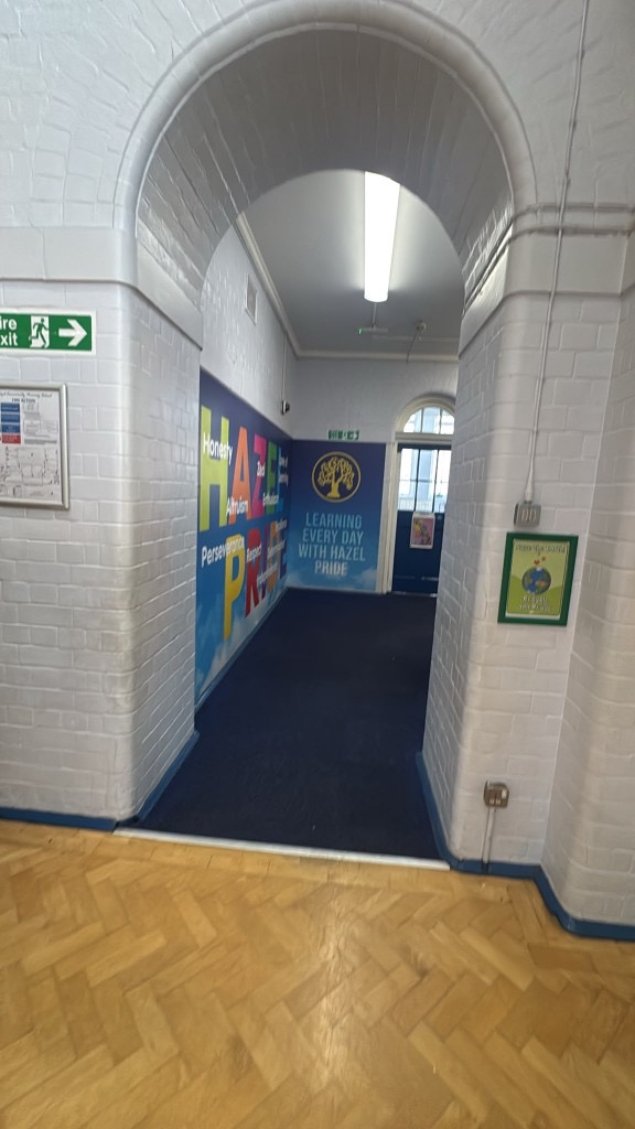 Freshly painted white brick archway looking into a Hazel Community Primary School corridor with blue carpet and Hazel Pride mural