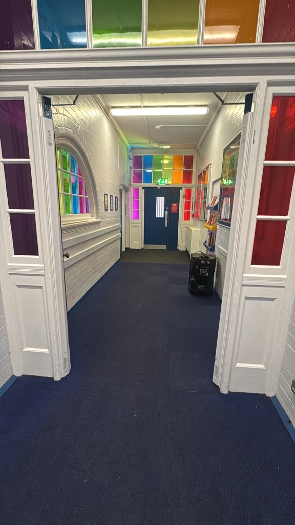 School corridor at Hazel Community Primary with white painted brick walls, coloured glass panels and blue carpet