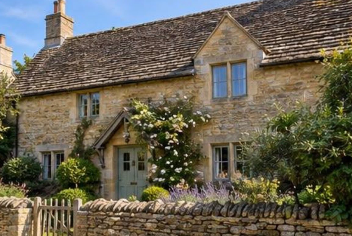 Honey-coloured stone cottage with sage green front door behind a dry stone wall