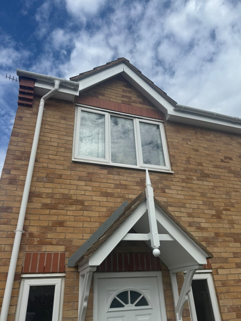White-painted porch canopy, fascia boards and soffits against brick and blue sky