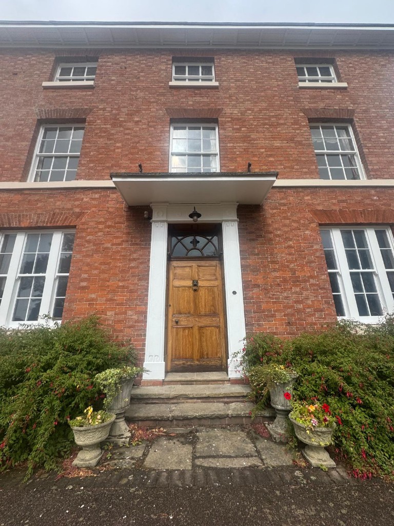 Front elevation of a 200-year-old red brick farmhouse with freshly painted white window frames, wooden front door and entrance canopy