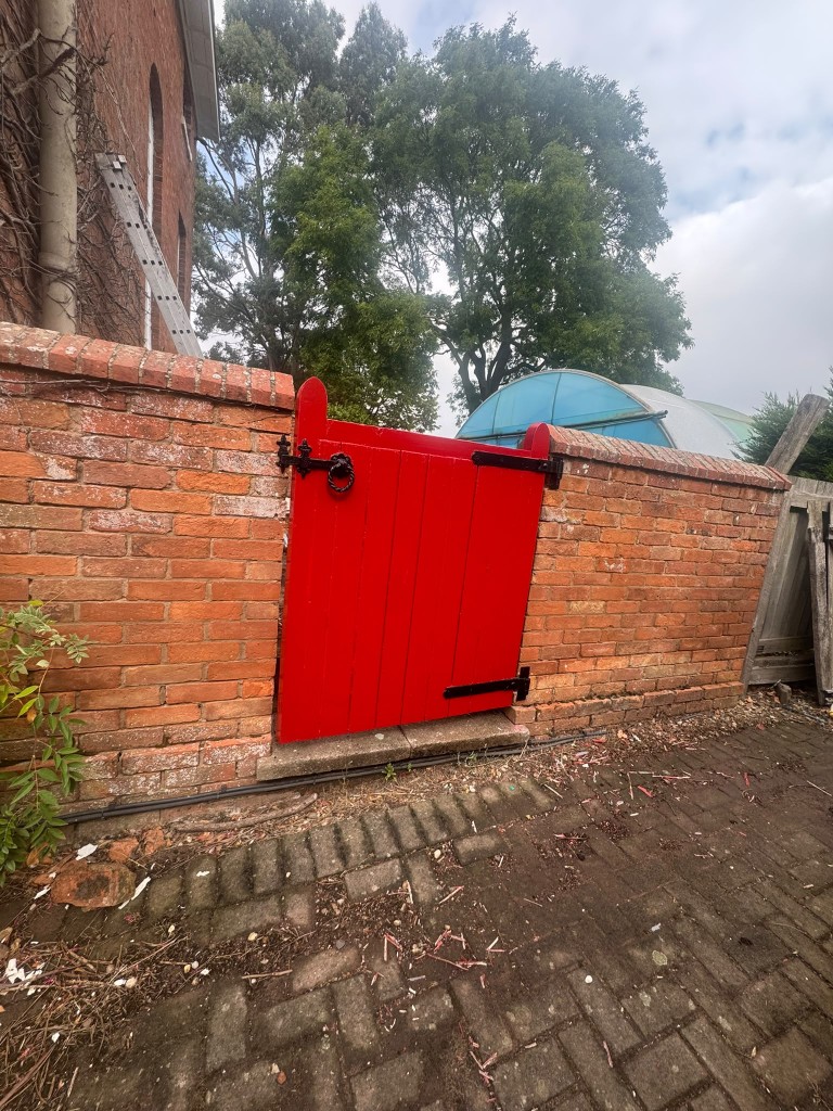 Newly painted red timber gate set in a weathered red brick garden wall at the farmhouse