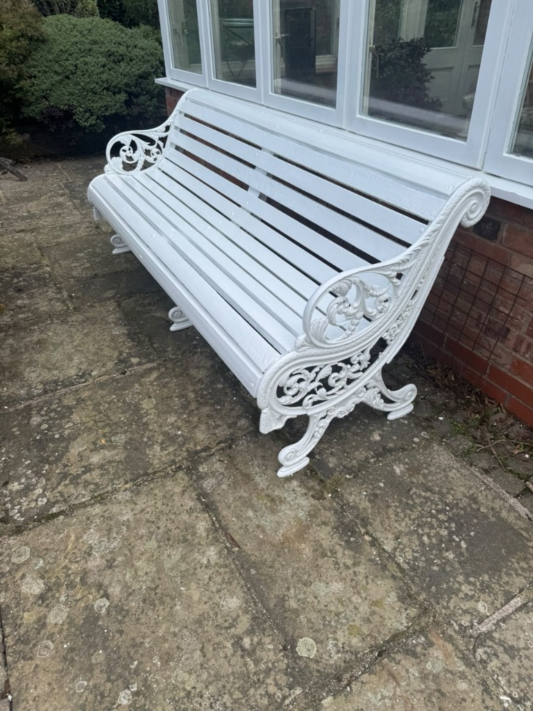 Ornate garden bench freshly painted white on a stone patio — after