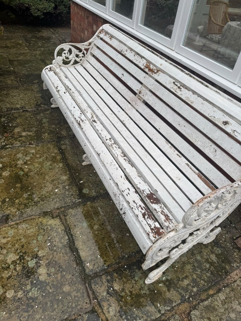 Same ornate garden bench with peeling white paint and rust — before restoration