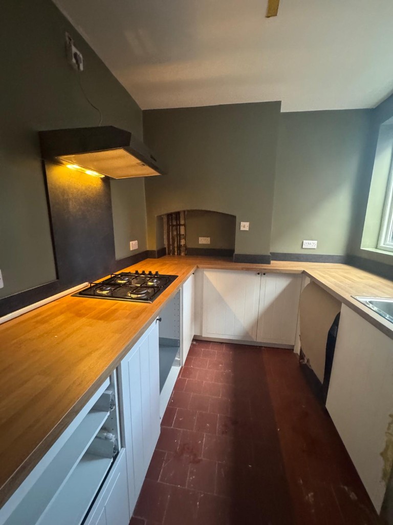 Sage green kitchen walls and wood worktops repainted in a housing association void