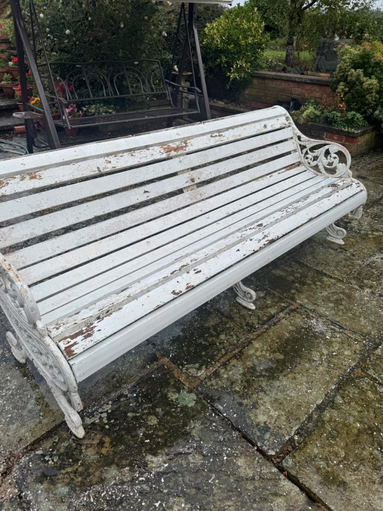 Weathered white garden bench with peeling paint on a mossy patio before jet cleaning
