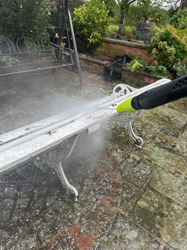 Pressure washing an ornate metal garden bench on a stone patio
