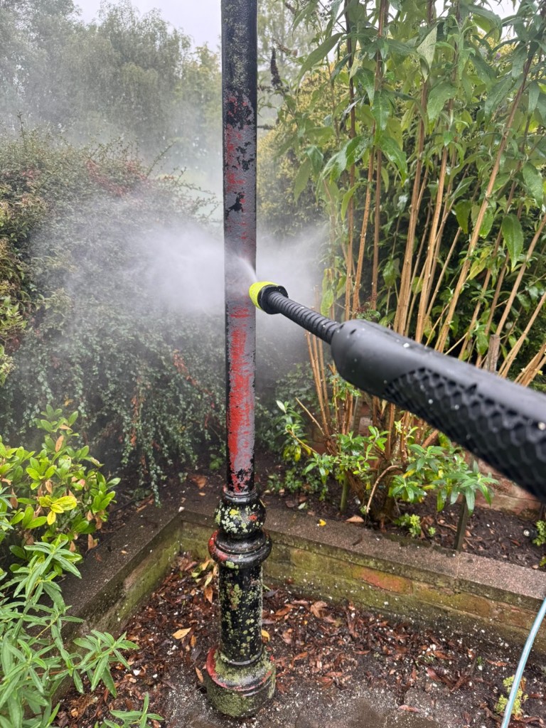 Jet cleaning a metal garden post — high-pressure spray removing moss and old paint