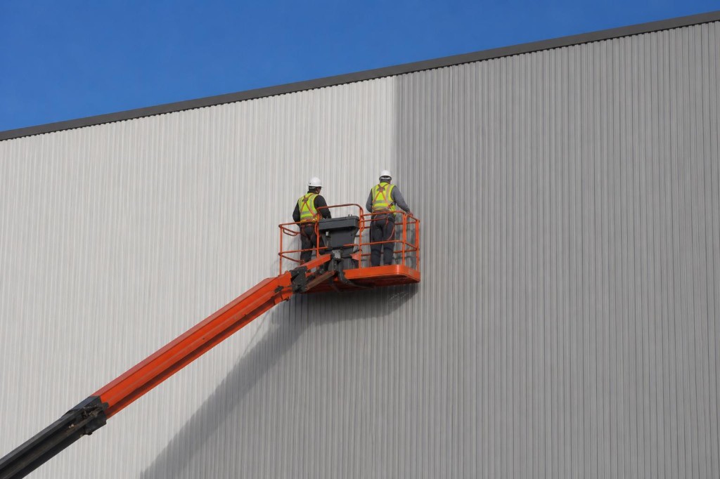 A.S Painting operatives in a cherry picker painting high-level industrial cladding on a commercial building in Leicestershire